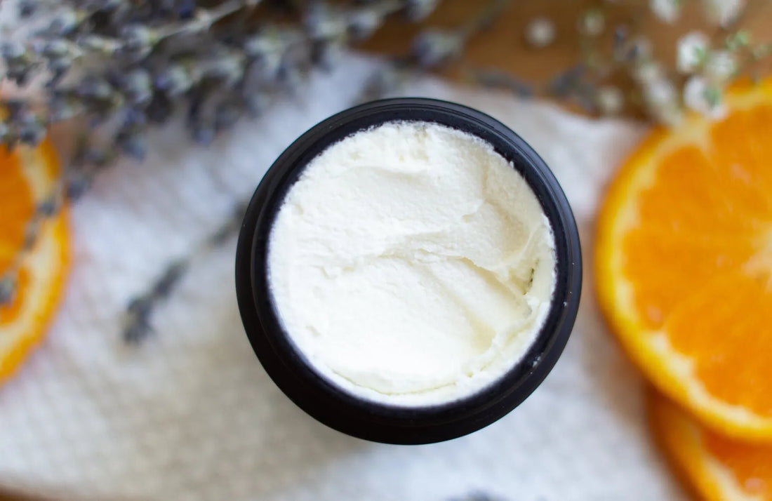 Top-down view of a black jar containing whipped white tallow products, surrounded by fresh orange slices and dried lavender sprigs.